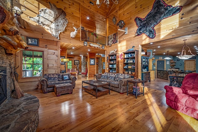 living area featuring wood walls, a towering ceiling, wood-type flooring, a chandelier, and a fireplace