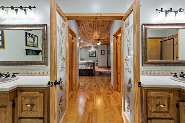 ensuite bathroom featuring wood finished floors, two vanities, and wooden ceiling