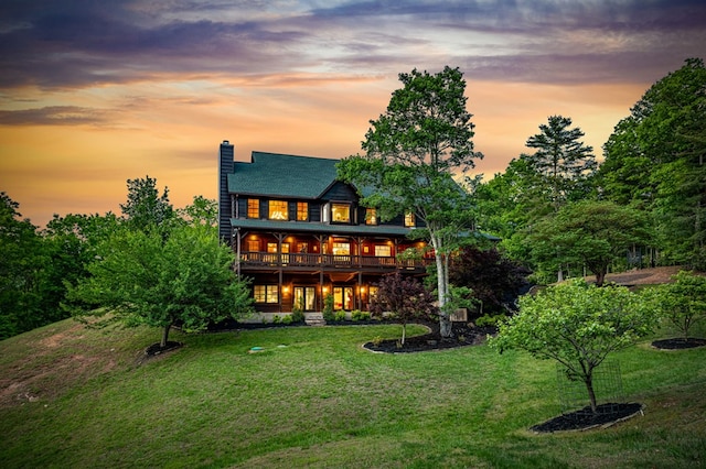 back of house at dusk with a lawn, a deck, and a chimney