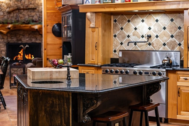 kitchen with stainless steel gas range, tasteful backsplash, a kitchen bar, a lit fireplace, and a sink