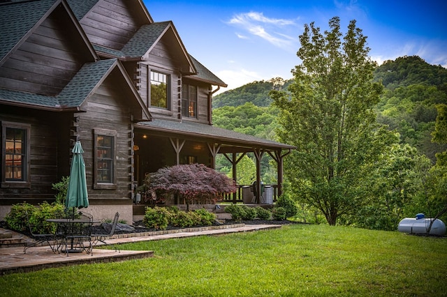 view of side of property featuring a yard, a shingled roof, and a patio area