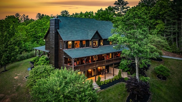 rear view of property featuring a chimney, a yard, a shingled roof, and a patio area