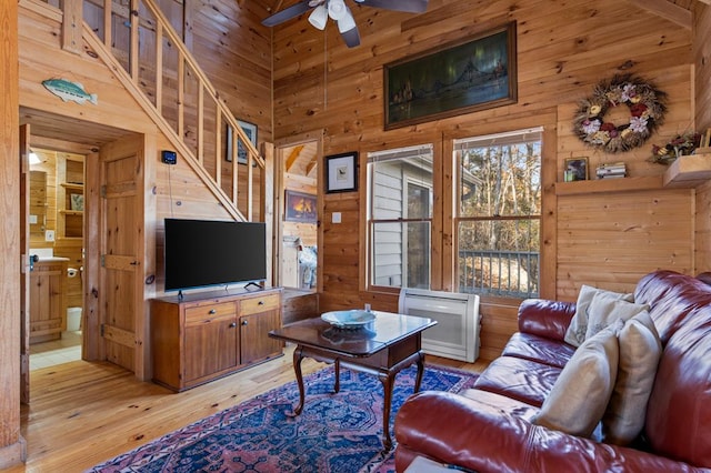 living room featuring ceiling fan, a towering ceiling, wooden walls, and light wood-type flooring