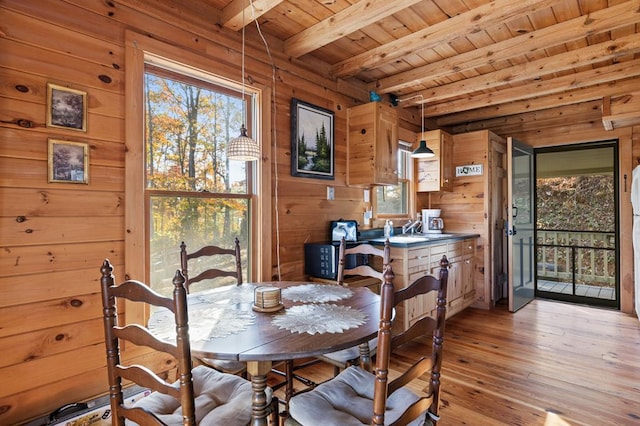 dining area with sink, wood walls, light hardwood / wood-style flooring, wooden ceiling, and beamed ceiling