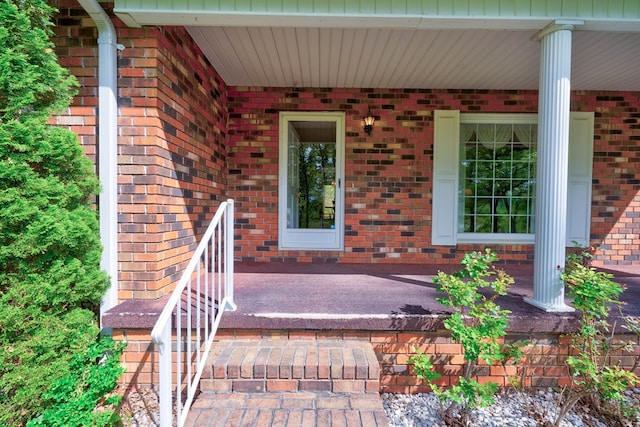 view of exterior entry featuring a porch and brick siding