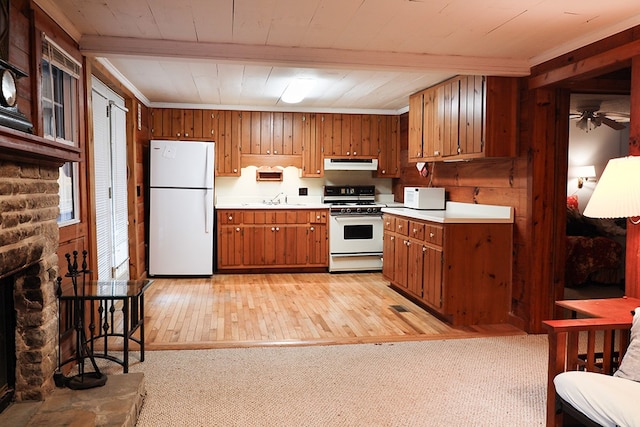 kitchen featuring white appliances, brown cabinets, under cabinet range hood, a fireplace, and a sink