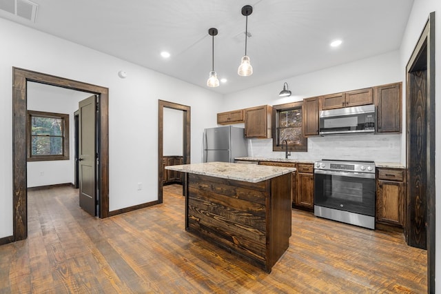 kitchen with a center island, sink, light stone countertops, decorative light fixtures, and stainless steel appliances