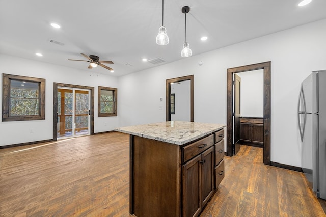 kitchen with pendant lighting, ceiling fan, stainless steel fridge, dark hardwood / wood-style floors, and light stone counters