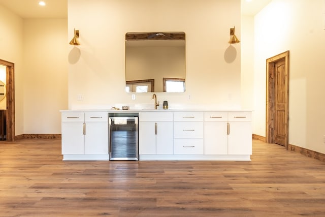 kitchen with baseboards, light wood-style flooring, a sink, wine cooler, and white cabinets