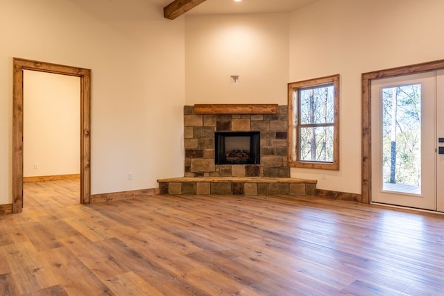 unfurnished living room with beamed ceiling, baseboards, a stone fireplace, and wood finished floors