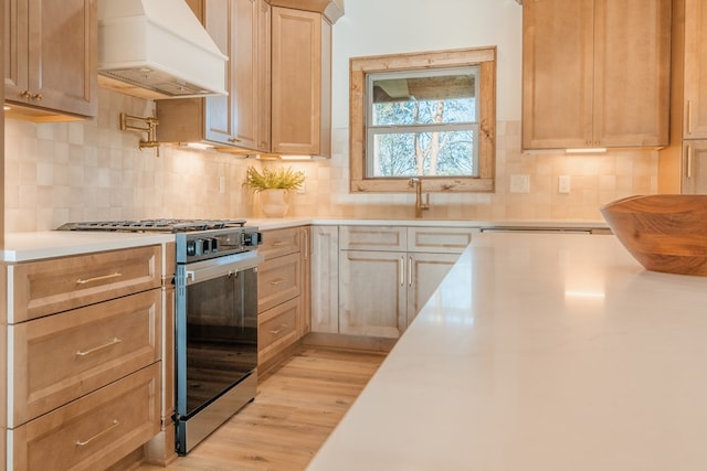 kitchen with premium range hood, stainless steel range with gas cooktop, light wood-style flooring, decorative backsplash, and light countertops