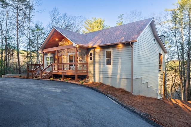 chalet / cabin with a deck, stone siding, and roof with shingles