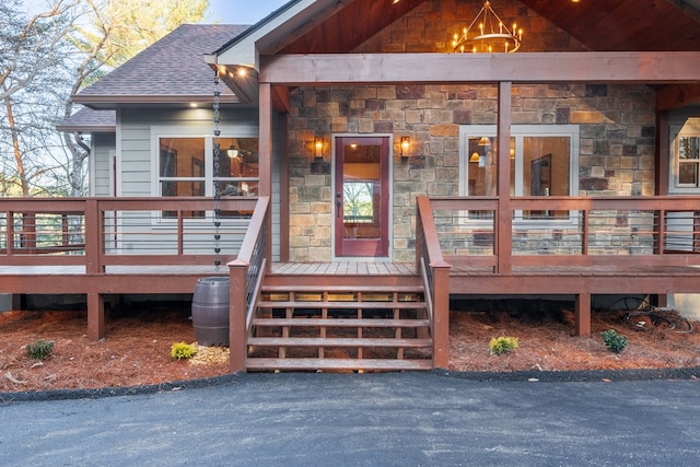 entrance to property featuring a deck, stone siding, and roof with shingles