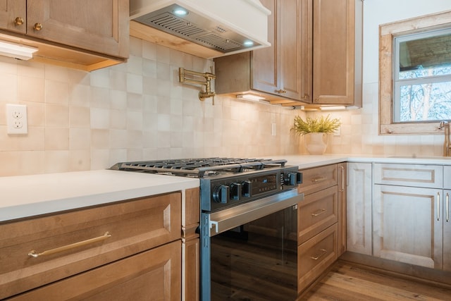 kitchen with decorative backsplash, range hood, light countertops, and gas range oven