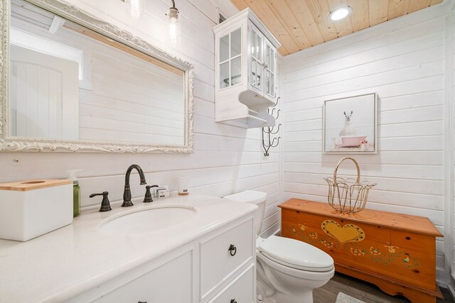 bathroom featuring wooden ceiling, hardwood / wood-style floors, toilet, wooden walls, and vanity