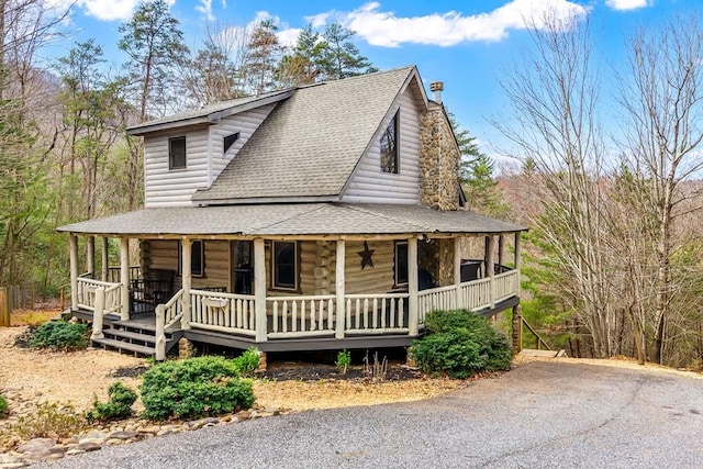 view of front of house with a porch, a chimney, and a shingled roof