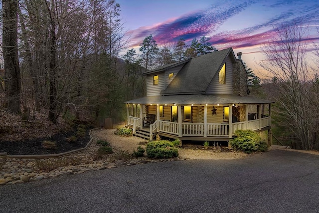 view of front of property with aphalt driveway, roof with shingles, covered porch, and a chimney