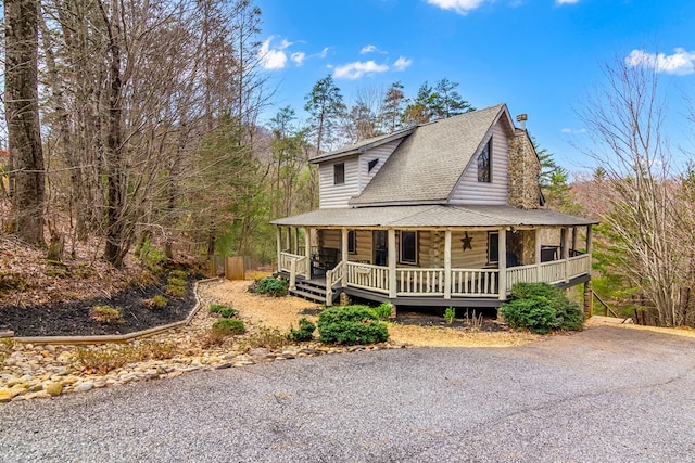 view of front of house featuring a porch, a chimney, and a shingled roof