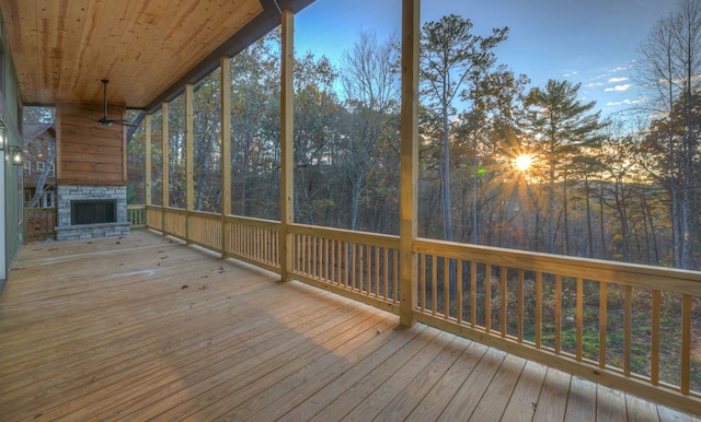 unfurnished sunroom featuring wooden ceiling, ceiling fan, and an outdoor stone fireplace