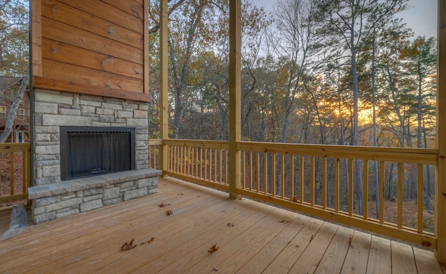 deck at dusk featuring an outdoor stone fireplace