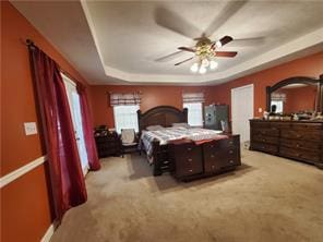 carpeted bedroom with multiple windows, a tray ceiling, and ceiling fan