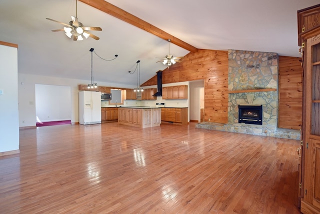 unfurnished living room with beamed ceiling, hardwood / wood-style floors, a stone fireplace, and wood walls