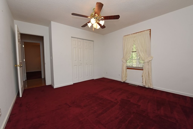 unfurnished bedroom featuring dark colored carpet, a textured ceiling, a closet, and ceiling fan