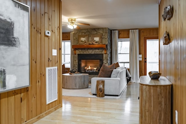 living room with a fireplace, light hardwood / wood-style floors, ceiling fan, and wooden walls