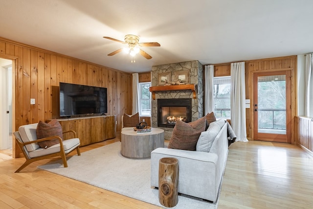 living room with ceiling fan, a fireplace, wood walls, and light wood-type flooring