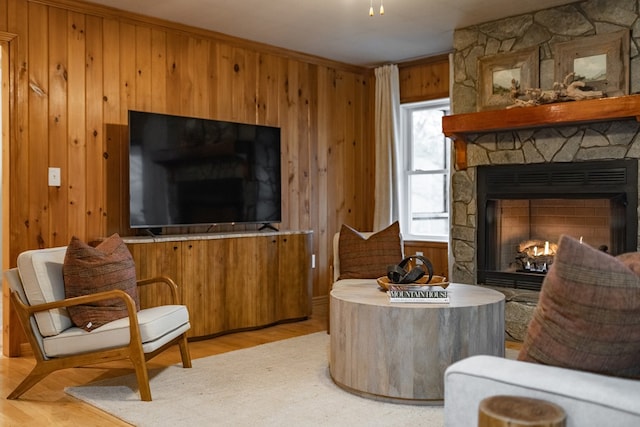 living area featuring a stone fireplace, light wood-type flooring, and wooden walls