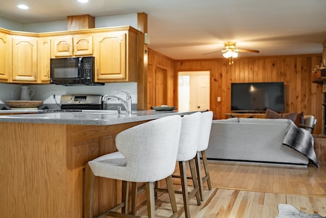 kitchen featuring wood walls, stove, light brown cabinetry, light hardwood / wood-style floors, and a breakfast bar area