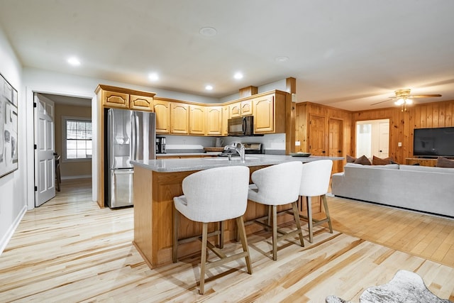 kitchen with wood walls, stainless steel fridge, a kitchen bar, and light hardwood / wood-style floors