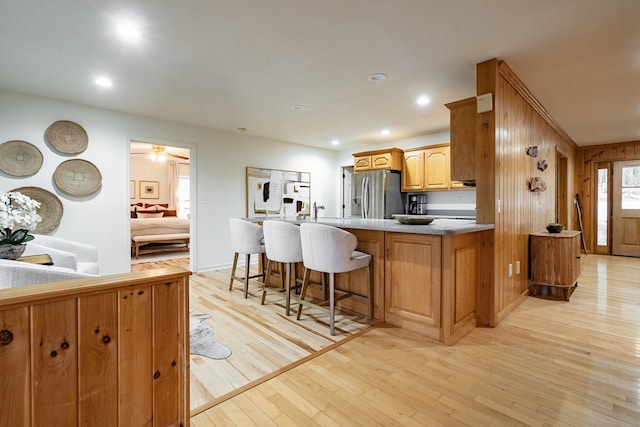 kitchen with kitchen peninsula, light wood-type flooring, a breakfast bar, wooden walls, and stainless steel fridge with ice dispenser