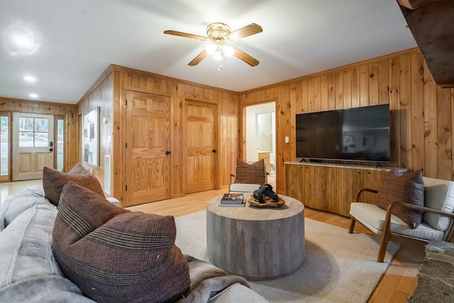 living room featuring ceiling fan, light hardwood / wood-style flooring, and wooden walls