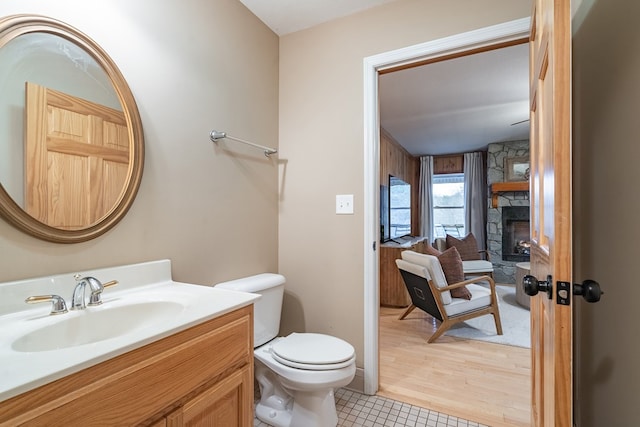 bathroom with toilet, vanity, a stone fireplace, and tile patterned flooring