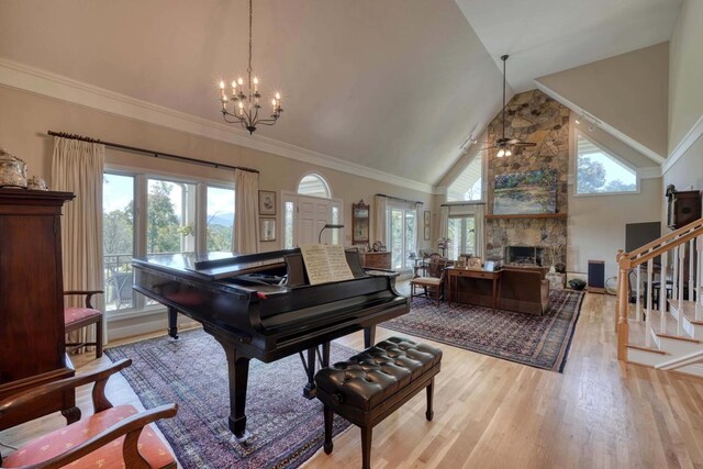 misc room with light hardwood / wood-style floors, ceiling fan with notable chandelier, high vaulted ceiling, a stone fireplace, and ornamental molding