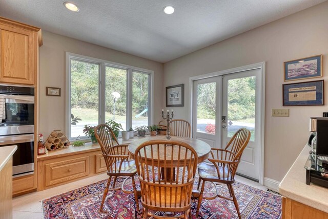 dining room featuring a textured ceiling, a healthy amount of sunlight, light tile patterned floors, and french doors