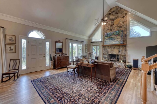 living room with high vaulted ceiling, a fireplace, wood-type flooring, crown molding, and ceiling fan