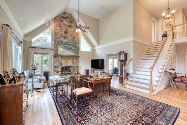 living room with ceiling fan with notable chandelier, wood-type flooring, high vaulted ceiling, and a fireplace