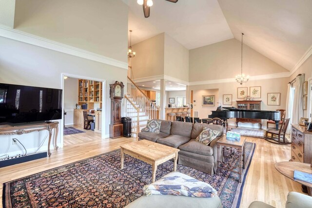 living room featuring ceiling fan with notable chandelier, light wood-type flooring, ornamental molding, and high vaulted ceiling