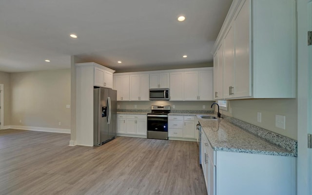 kitchen with light stone counters, white cabinetry, sink, light hardwood / wood-style floors, and stainless steel appliances