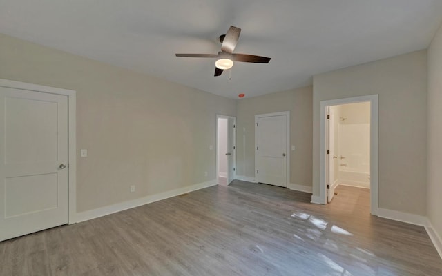 unfurnished bedroom featuring ensuite bath, ceiling fan, baseboards, and wood finished floors