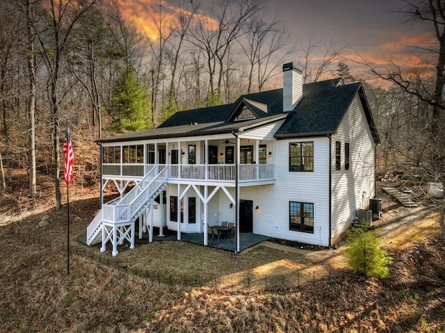 back of property at dusk with ceiling fan, stairway, a chimney, a sunroom, and a patio area