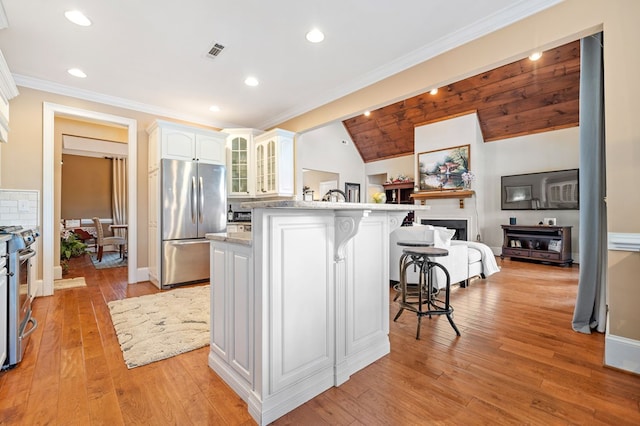 kitchen featuring visible vents, stainless steel appliances, glass insert cabinets, a kitchen breakfast bar, and light wood-type flooring