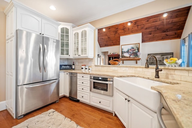 kitchen with a sink, decorative backsplash, stainless steel appliances, glass insert cabinets, and light wood-type flooring