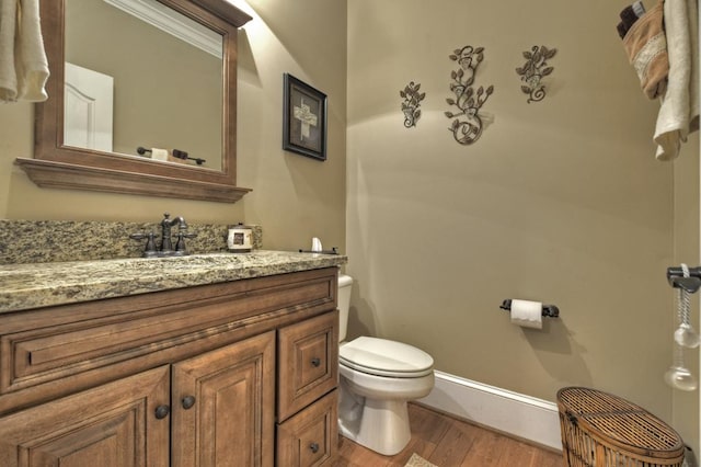 half bathroom with toilet, vanity, baseboards, and wood finished floors