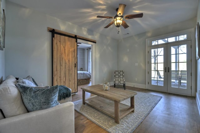 living room with a ceiling fan, wood finished floors, a barn door, french doors, and baseboards