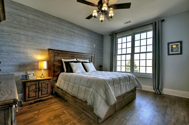 bedroom with visible vents, an accent wall, baseboards, and wood finished floors