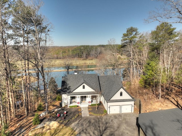 view of front of property featuring driveway, roof with shingles, a garage, and a water view