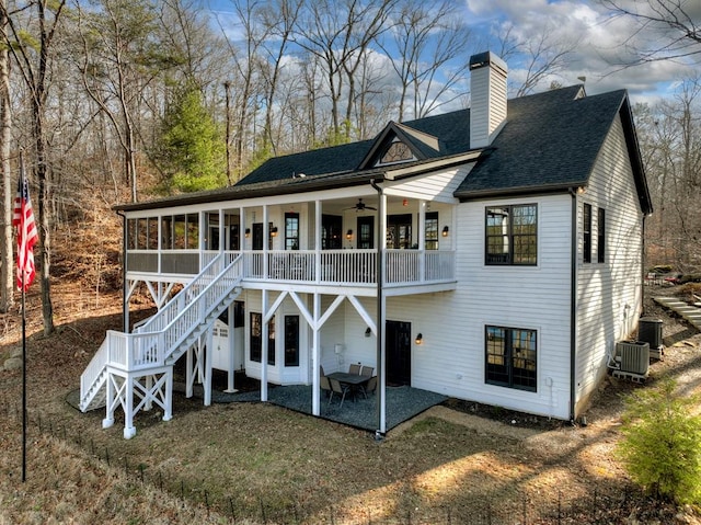 back of house featuring a shingled roof, stairs, a chimney, a sunroom, and a patio area